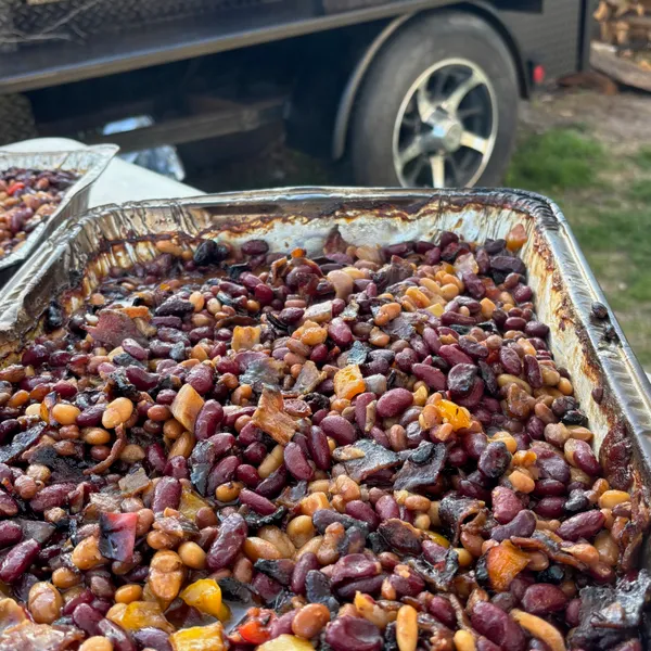 A tray of smokey bacon baked beans with the smoker trailer behind it