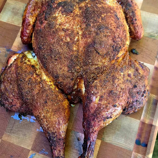 A whole smoked chicken, halved, resting on the cutting board