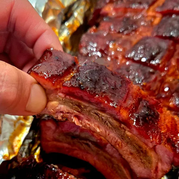 A glazed rib bone held up, showing off the smoke ring