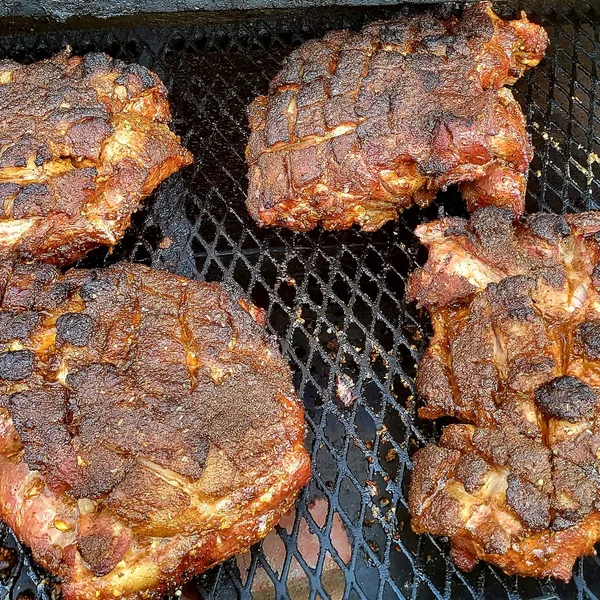 Seasoned pork steaks, scored and smoking on the grate